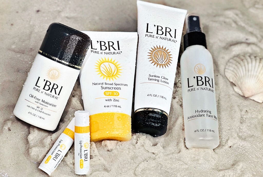 L'BRI Sun Care products laying on a sandy beach with seashell